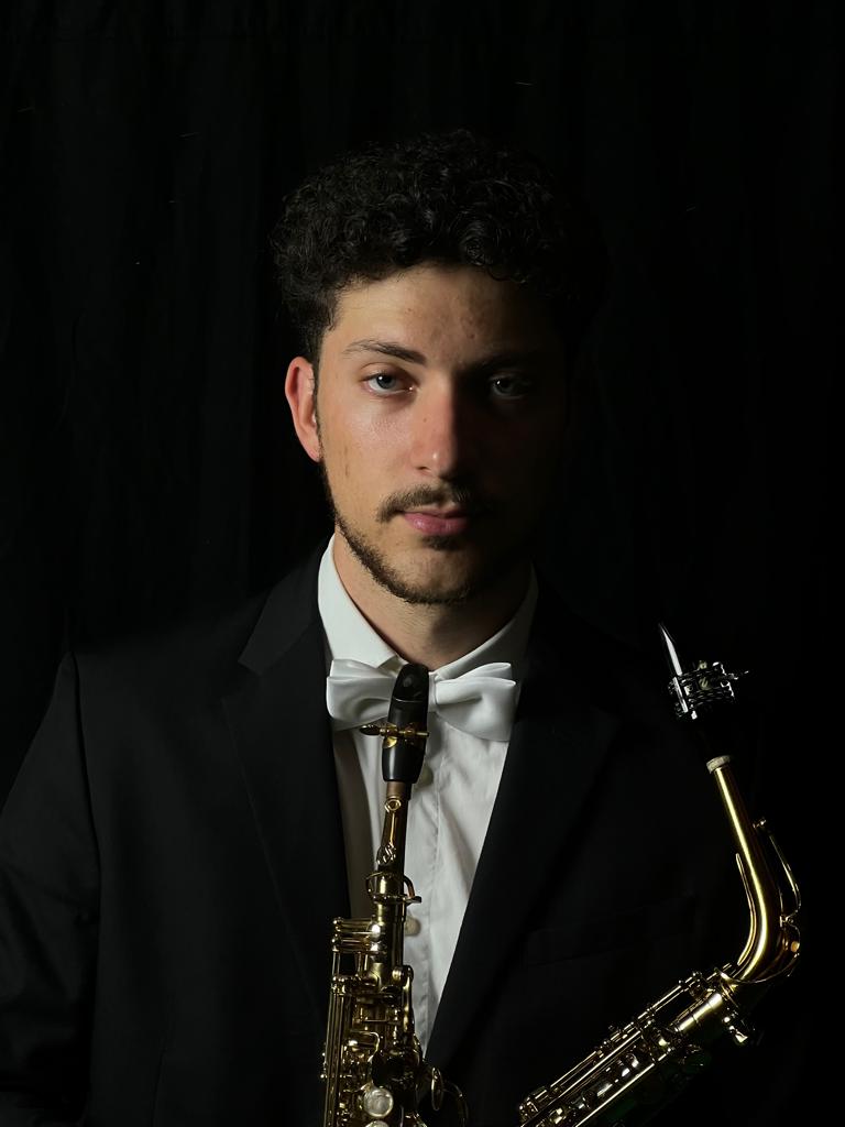 Photo of João Luís holding his alto saxophone, dressed in a suit for playing at an event