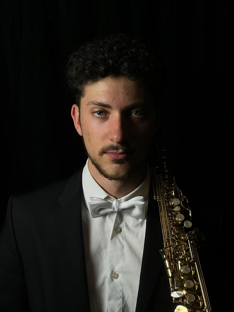 Photo of João Luís holding his soprano saxophone, dressed in a suit for playing at an event